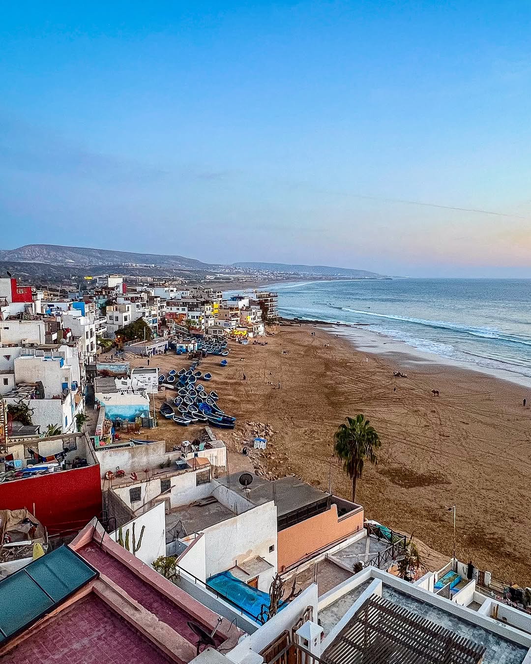 Taghazout fishing village at dusk with stacked blue boats and painted houses on the Atlantic shore, Morocco