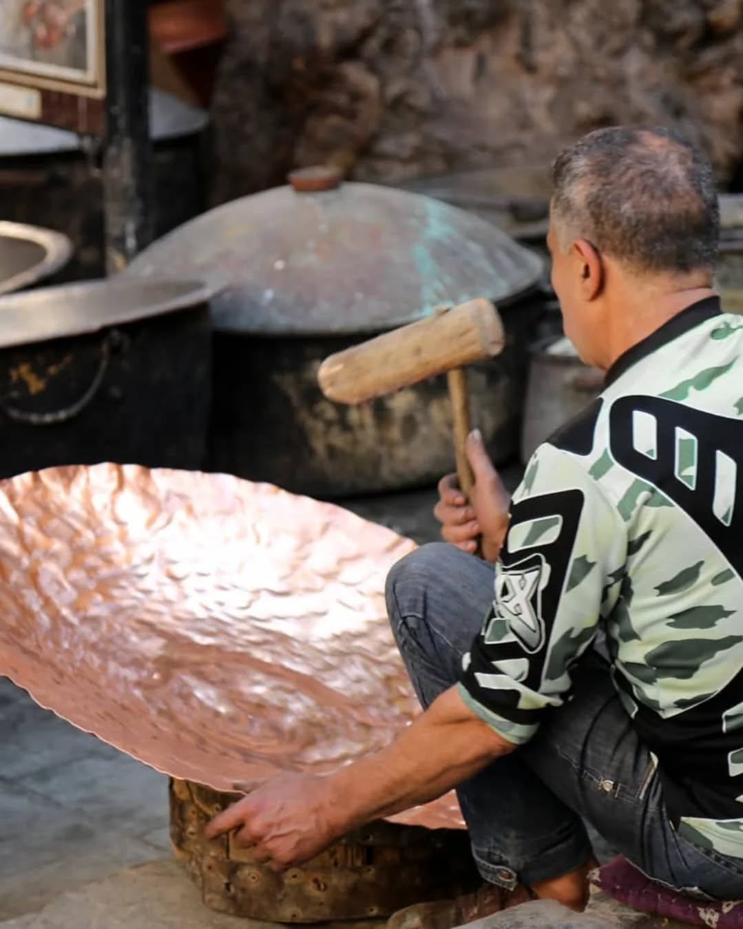 Hand-Hammered Copper Fes coppersmith hammering a copper plate over a wooden anvil