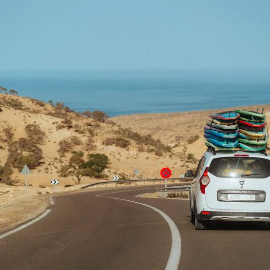 White Dacia Duster SUV with surfboards on the roof rack driving along the Atlantic coast road in Morocco