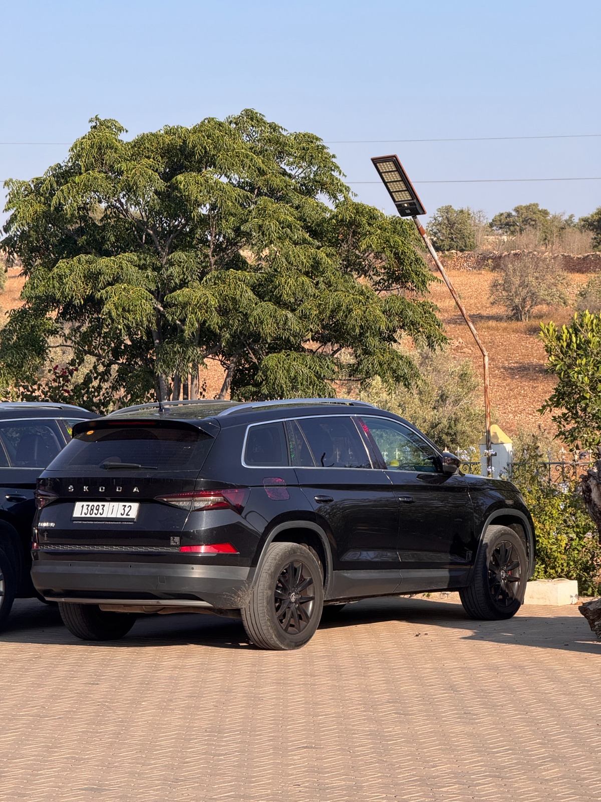 Rear three-quarter view of a black Škoda Kodiaq parked under trees in the Moroccan countryside