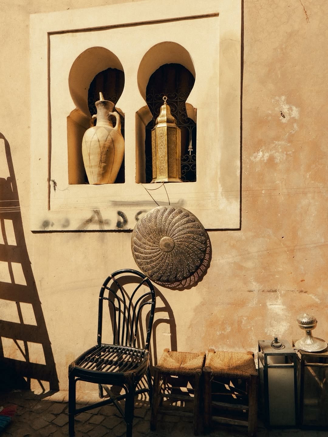 Riad Courtyard Sunlit riad wall with arched niches, vase and brass lantern in Marrakech
